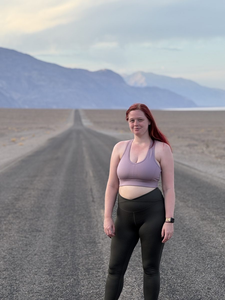 Jenna standing on an empty desert road with mountains in the distance