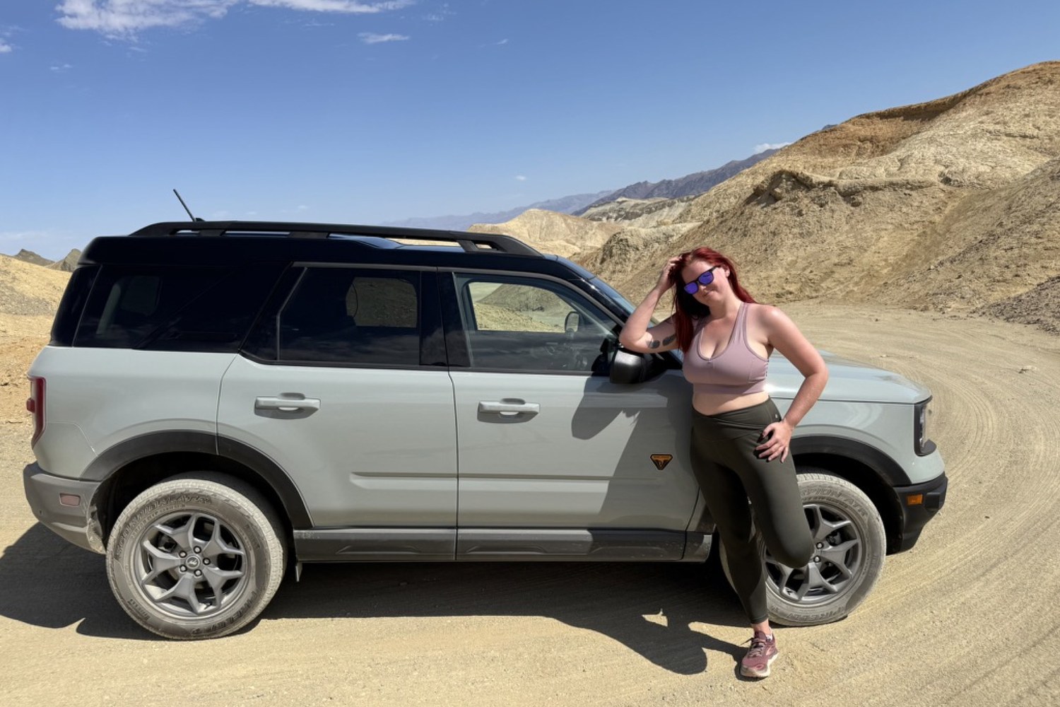Leaning against Daisy the Bronco on a desert road, badlands rising behind